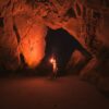 man holding red light flare inside cave