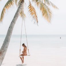 woman wearing bikini sitting on swing near coconut tree