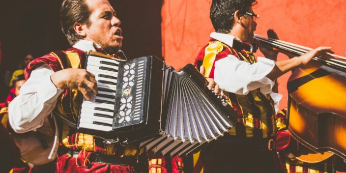 two men playing cello and accordion beside red building photo