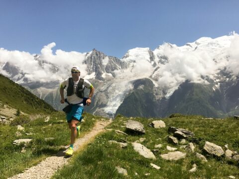 man in white shirt and blue shorts running on brown ground between green grass during daytime